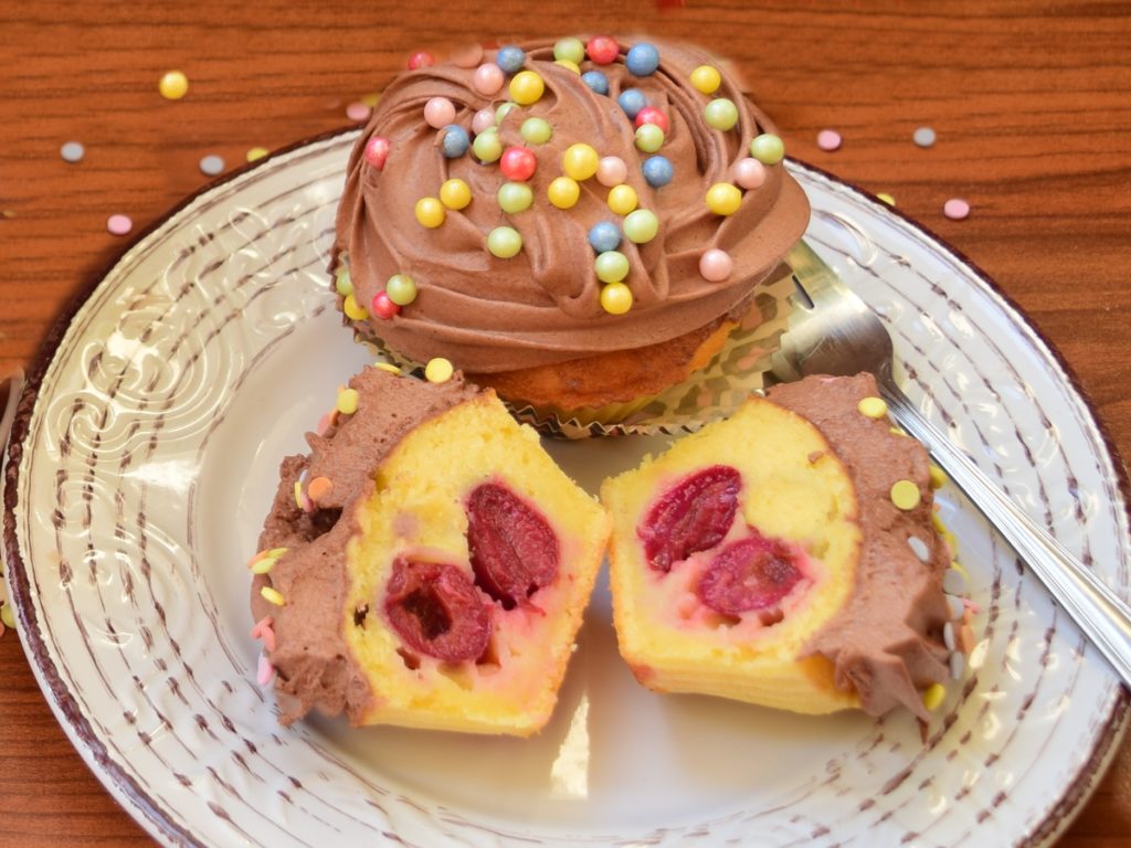 Două cupcakes vanilate cu iaurt și vișine, una secționată pe jumătate