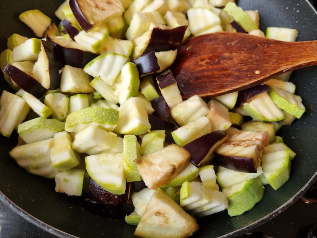 Bucăți de vânătă și dovlecel în tigaie cu spatulă de lemn