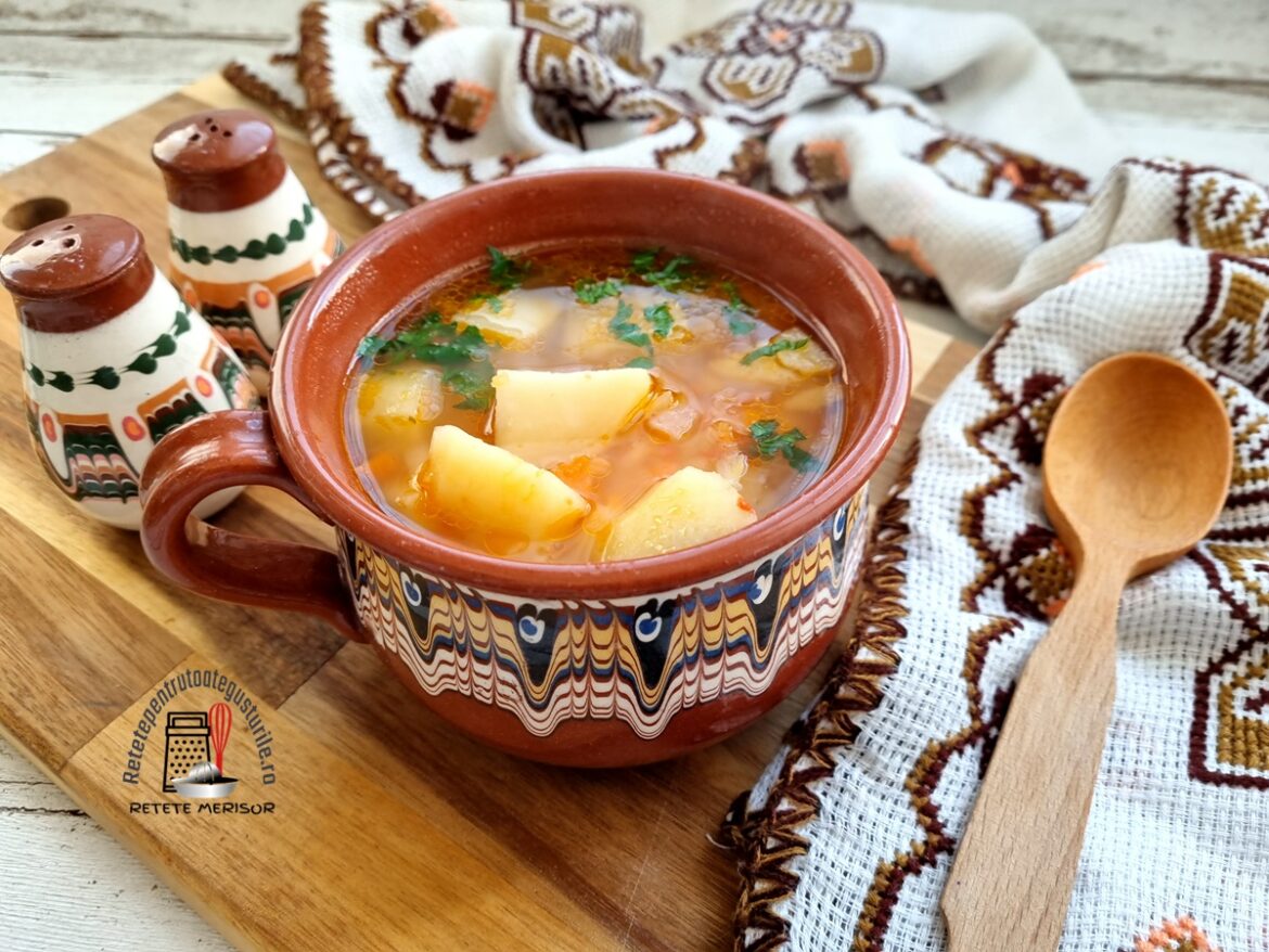 Bol rustic cu porție de ciorbă de cartofi cu zeamă de varză pe un tocător, cu un ștergar rustic, lingură de lemn și două solnițe