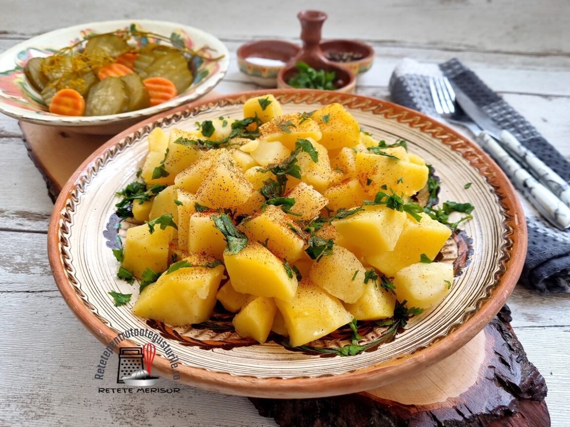 Cartofi natur de post pe un platou rustic, alături de o farfurie rustică cu murături, o solniță și tacâmuri pe un ștergar