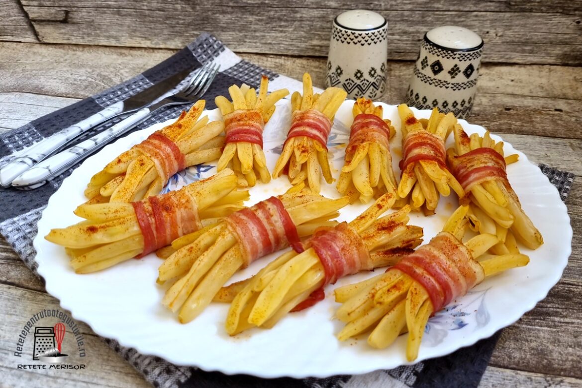 Buchete de păstăi galbene în bacon afumat pe un platou alb, alături de două solnițe