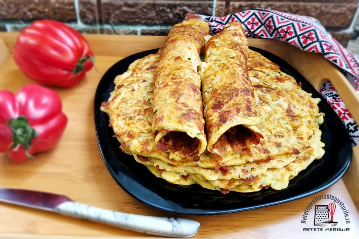 Clătite de dovlecel cu mozzarella și șuncă presată pe o farfurie neagră, două clătite rulate, alături de două roșii mari și un cuțit