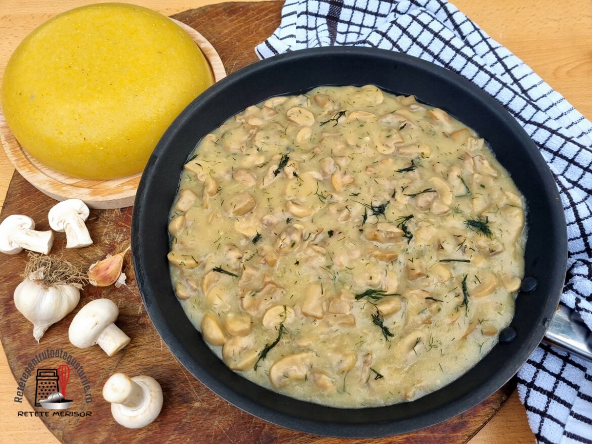 Ciulama de ciuperci în tigaie, alături de mămăliguță pe un platou de lemn și ciuperci cu usturoi, toate pe un tocător de lemn rustic