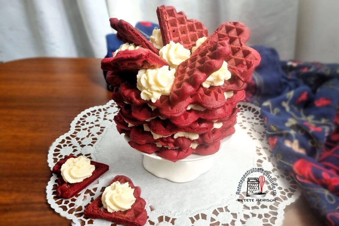 Tortuleț din vafe red velvet cu cremă de cocos pe un platou alb cu picior, alături de două vafe inimioară cu cremă