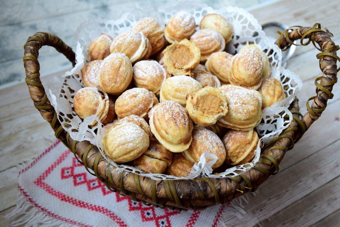 Nuci cu cremă caramel și miez de nuci decorate cu zahăr pudră, una secționată, într-un coș împletit
