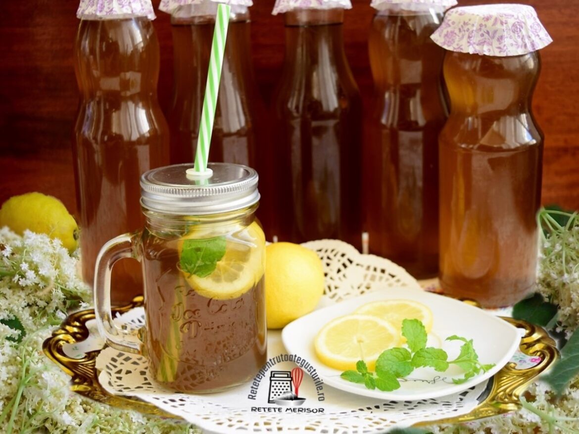 Sirop din flori de soc în sticle și într-un borcan cu pai, alături de lămâi, frunze de mentă și flori de soc