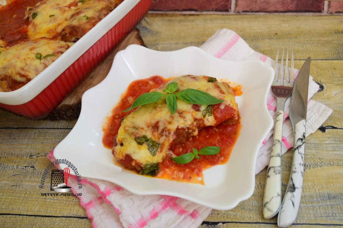 Porție de pui cu parmezan și mozzarella pe o farfurie albă, alături de cuțit și furculiță și vasul cu restul preparatului